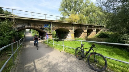 Fahrradfahrer mit Helm fährt unter einer alten Eisenbahnbrücke durch
