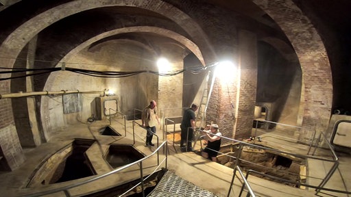 Das Bild zeigt ein beleuchtetes Kellergewölbe mit mehreren Becken, in denen das Aachener Thermalwasser aus der Erde kommt