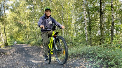 Jugendlicher mit Helm auf dem Kopf fährt mit einem Mountainbike durch einen Wald