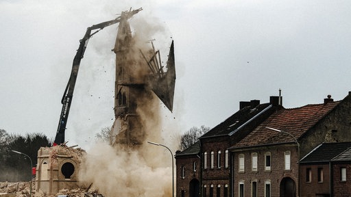 Der letzte Turm des Immerather Doms Sankt Lambertus wird abgerissen. Dabei fällt gerade die Turmspitze auf den Boden. Rechts davon leerstehende Wohnhäuser.