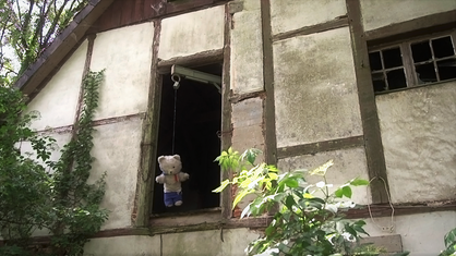 Ein Teddybär hängt vor einem heruntergekommenen Gebäude.