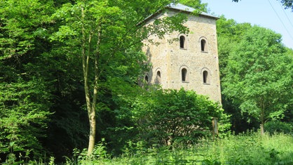 Ein aus Ruhrsandstein gemauerter ehemaliger Fördertum, inmitten von Bäumen und Sträuchern im Weitmarer Holz