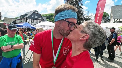 Manuela und Marco Peetz küssen sich nach dem Zieleinlauf beim Bödefelder Hollenmarsch. Marco Peetz trägt eine Medaille.