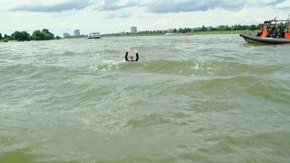 Ein Schwimmer im Rhein hat die Arme gehoben und winkt.