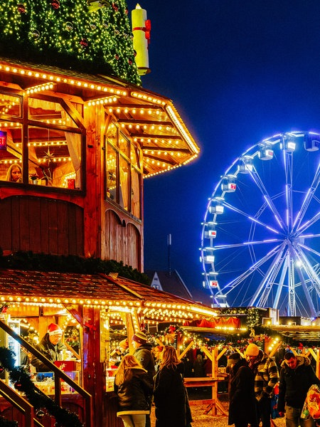 Der Weihnachtsmarkt Cranger Weihnachtszauber mit gut besuchten Ständen im Vordergrund und einem blau beleuchteten Riesenrad im Hintergrund.