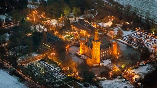 Luftansicht vom Weihnachtsmarkt am frühen Abend auf dem erleuchteten Schloss Moyland.