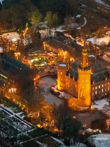 Luftansicht vom Weihnachtsmarkt am frühen Abend auf dem erleuchteten Schloss Moyland.