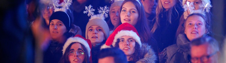 Junge Frauen mit Weihnachtsmützen und Schneeflocken auf dem Kopf singen bei "Loss mer Weihnachtsleeder singe" im Stadion in Köln