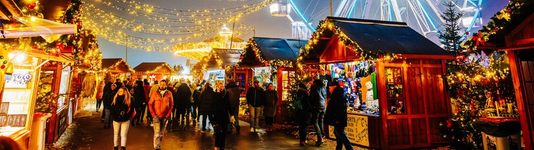 Blau leuchtendes Riesenrad auf dem Herner Weihnachtsmarkt hinter Weihnachtsmarktständen