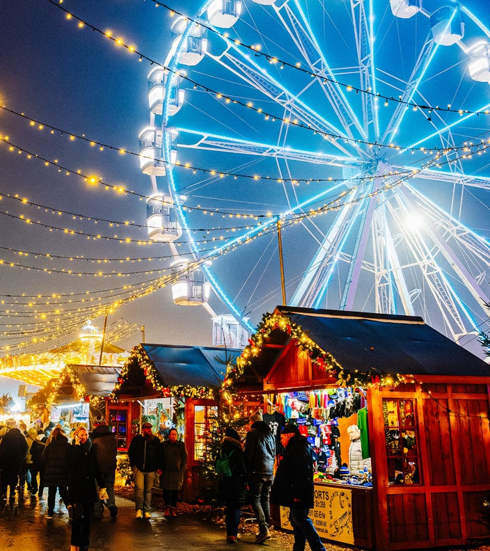 Blau leuchtendes Riesenrad auf dem Herner Weihnachtsmarkt hinter Weihnachtsmarktständen