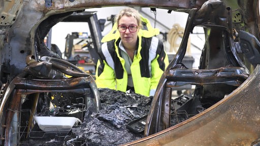 Brandermittlerin Julia Daams guckt in ein ausgebranntes Autowrack