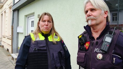 Eine Frau mit braunen Haaren in greller Polizeiuniform. Neben ihr ein Mann mit Bart, ebenfalls in Uniform.