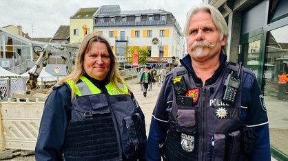 Ein Mann mit Bart in blauer Polizeiuniform. Daneben eine Frau mit braunen Haaren ebenfalls in Uniform.