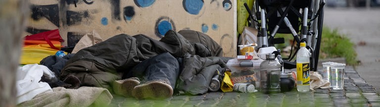 Eine Person liegt in einem Schlafsack auf einem Bürgersteig