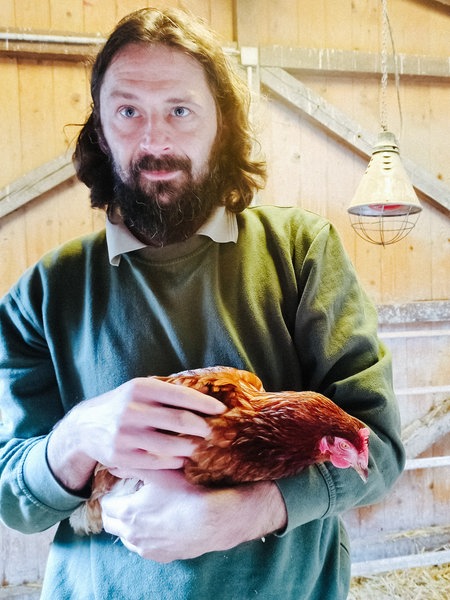 Patrick Scheddies hält ein Huhn in seinem Arm. 