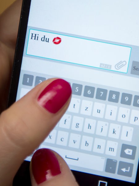 Eine Frau tippt auf einem Smartphone "Hi du" und einen Kussmund ein
