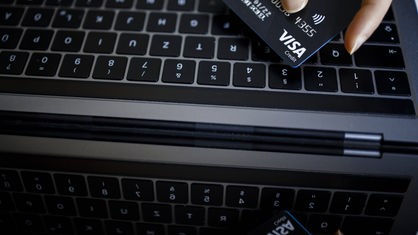 Eine Kreditkarte vom Typ VISA Card wird neben einer Computertatstatur gehalten.