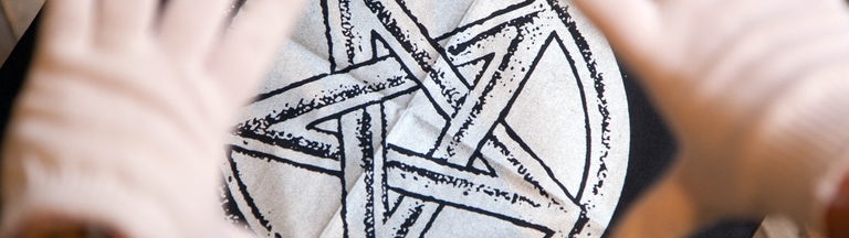 Das Bild zeigt einen fünfzackigen schwarz-weißen Stern auf einem schwarzen Stück Stoff, darüber zwei Hände in weißen Handschuhen.