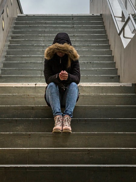 Eine Jugendliche sitzt mit gesenktem Kopf auf einer Treppe, sie trägt eine Kaputze.