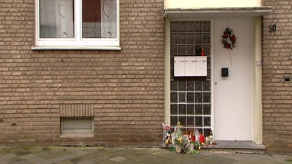 Das Bid zeigt die bräunliche Außenfassade des Hauses, in dem die Familie von Mark S. gewohnt hat. Vor der Haustür stehen Kerzen und Blumen.