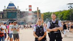 Eine Polizistin und ein Polizist stehen vor einem großen Gebäude, auf dem "Parookaville" steht