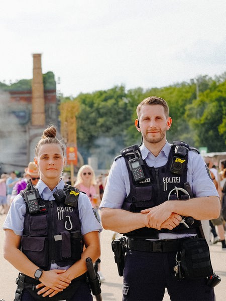Eine Polizistin und ein Polizist stehen vor einem großen Gebäude, auf dem "Parookaville" steht