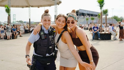 Zu sehen ist eine Polizistin, die mit zwei Besucherinnen posiert