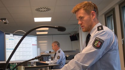 Mann mit rotblondem Haar und Bart in Polizeiuniform mit Headset auf dem Kopf schaut auf einen Computerbildschirm