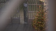 Ein Gittertor mit der Aufschrift "Kein Durchgang". Vor dem Gitter steht ein Weihnachtsbaum mit Lichterketten und roten Christbaum-Kugeln.