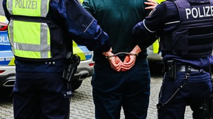 Symbolbild: Ein Mann wird von der Polizei mit Handschellen abgeführt. 