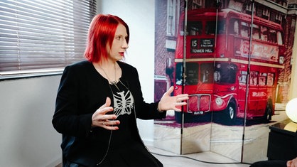 Eine Frau mit roten Haaren innerhalb eines Raumes. Im Hintergrund ein Wandbild mit einem roten Doppeldeckerbus