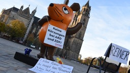  Die von Aktivisten der Kampagnenorganisation Campactin Köln entführte Maus aus der Sendung mit der Maus steht mit Schildern auf dem Domplatz.