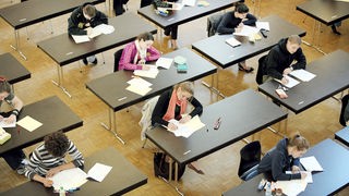 Schüler sitzen in einem Klassenraum an getrennten Tischen und schreiben eine Prüfung
