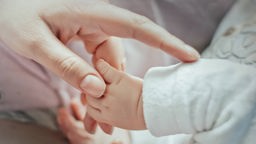 Ein neugeborenes Baby hält die Hand seiner Mutter.