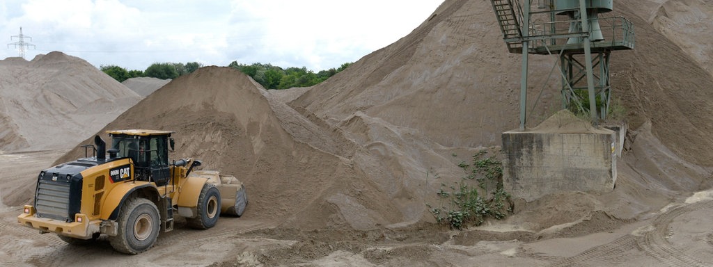 Das Beitragsbild des Dok 5 Feature "Auf Sand gebaut - Konlikt um Sand und Kies", zeigt ein Kieswerk mit Bagger und Förderturm