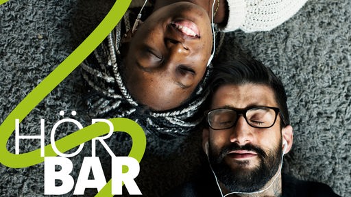 Eine Frau und ein Mann liegen Kopf an Kopf auf einem Teppich und hören genussvoll Musik über Kopfhörer