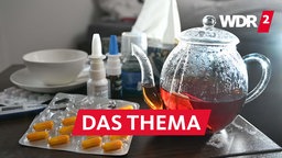 Medikamente und eine Kanne und Tasse Tee zur sind auf einem Nachttisch aufgestellt.