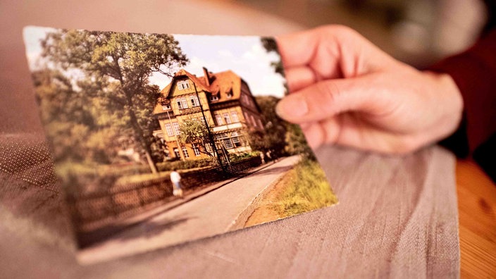 Sabine Schwemm, die als Kind in die Kinderheilanstalt "Waldhaus" Bad Salzdetfurth geschickt wurde, hält in ihrer Hand eine historische Postkarte der Heilanstalt.