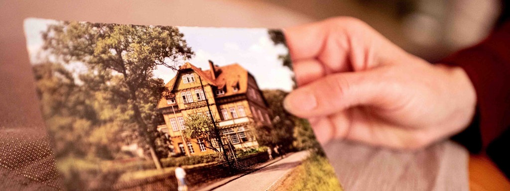 Sabine Schwemm, die als Kind in die Kinderheilanstalt "Waldhaus" Bad Salzdetfurth geschickt wurde, hält in ihrer Hand eine historische Postkarte der Heilanstalt.