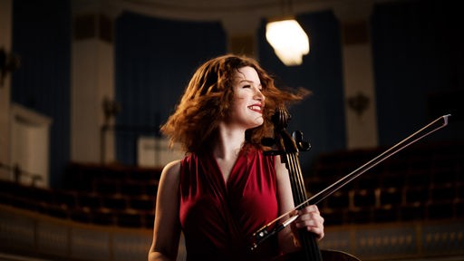 Die Cellistin Julia Hagen hält ihren Bogen in der Hand und blickt lächelnd zur Seite.