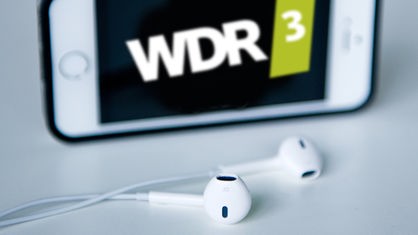 Kopfhörer liegen vor einem iPhone mit WDR 3 Sendelogo