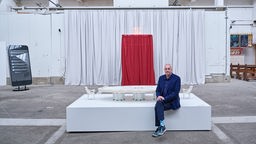 Julian Kirschler sitzt vor seiner Kunstinstallation "DER TISCH".