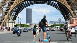 Eine Person fährt auf einem E-Scooter, Im Hintergrund der Eifelturm in Paris.