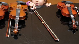 Ein Kind greift nach einem Bogen, der zwischen Geigen liegt.