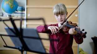 Ein Kind spielt auf einer Geige und ließt Noten von einem Tablet ab.