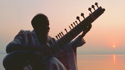 Symbolbild: ein Mann spielt bei Sonnenuntergang auf einer Sitar.