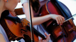 Zwei Personen spielen auf einer Geige (l.) und einem Cello (r.).