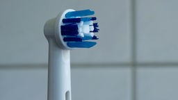 Eine elektrische Zahnbürste der Marke "Oral-B" steht vor weißen Kacheln