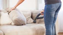 Eine junge Frau saugt in einer Wohnung in Hamburg mit einer speziellen Polsterduese ein Sofa ab.