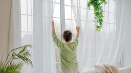 Eine Frau öffnet die Vorhänge des Fensters zu Hause.